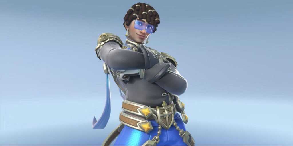 Lucio in stylish black and blue attire, confidently posing with arms crossed, showcasing intricate accessories against a light backdrop.