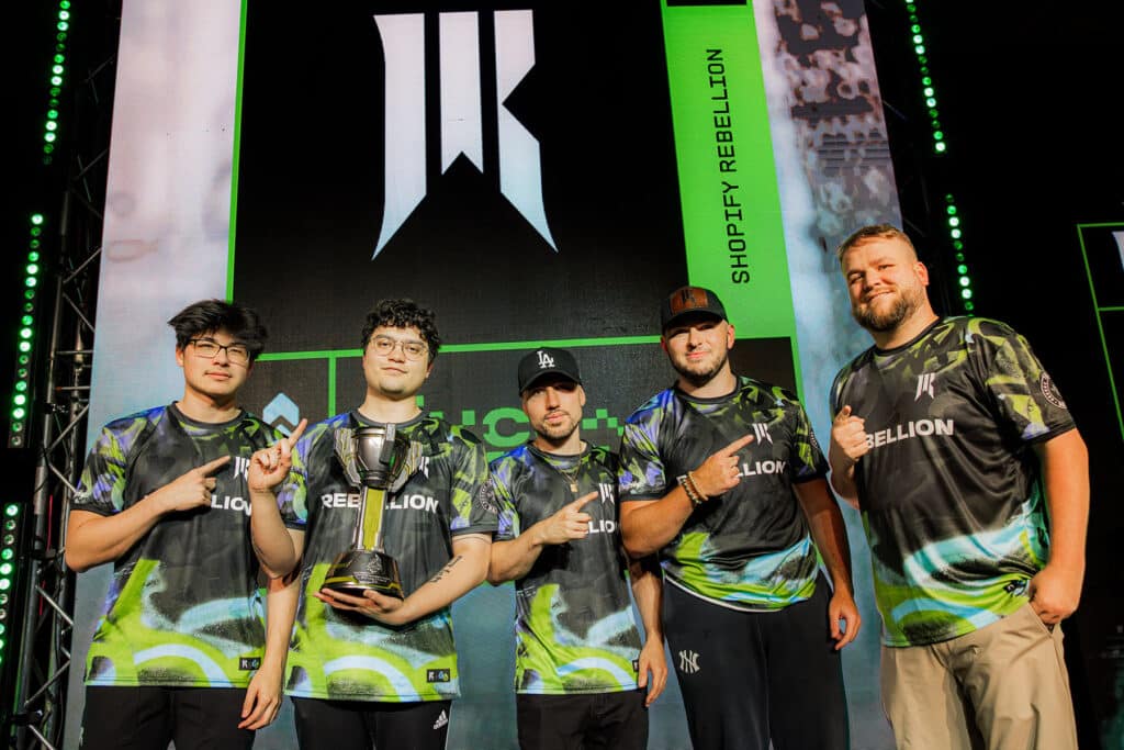 Image of Shopify Rebellion Halo roster posing on stage with HCS Salt Lake city trophy. The Shopify Rebellion logo is showing on a screen in the background